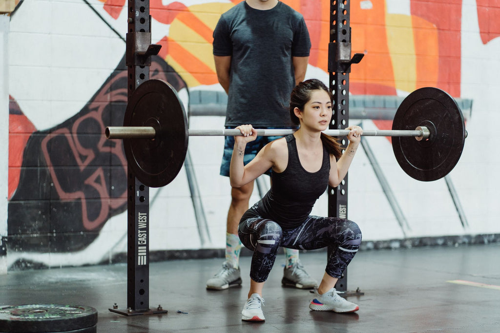 Persona haciendo sentadilla con barra en el gym